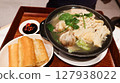 close up of a Singaporean white pepper soup Bak kut teh with pork rib, garlic, Flammulina filiformis in a black clay pot, spicy chili soy sauce and Chinese Fried Dough Sticks in a wooden tray 127938022