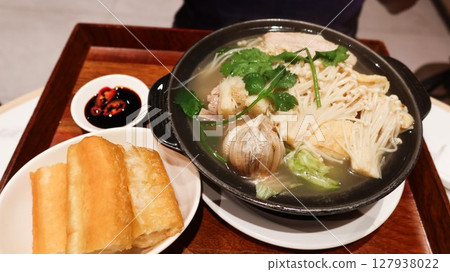 close up of a Singaporean white pepper soup Bak kut teh with pork rib, garlic, Flammulina filiformis in a black clay pot, spicy chili soy sauce and Chinese Fried Dough Sticks in a wooden tray close up of a Singaporean white pepper soup Bak kut teh with pork rib, garlic, Flammulina filiformis in a black clay pot, spicy chili soy sauce and Chinese Fried Dough Sticks in a wooden tray 127938022