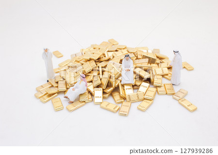 Miniature Figures Standing Around Pile of Shiny Gold Bars 127939286