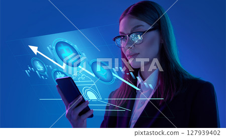 Businesswoman analyzing cryptocurrency trends on smartphone with futuristic blue holograms Businesswoman analyzing cryptocurrency trends on smartphone with futuristic blue holograms 127939402