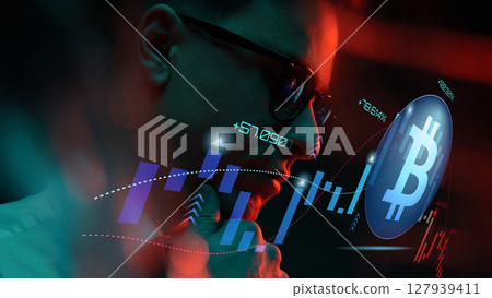 Trader analyzing bitcoin market trends on digital screen in dimly lit environment with red lighting 127939411
