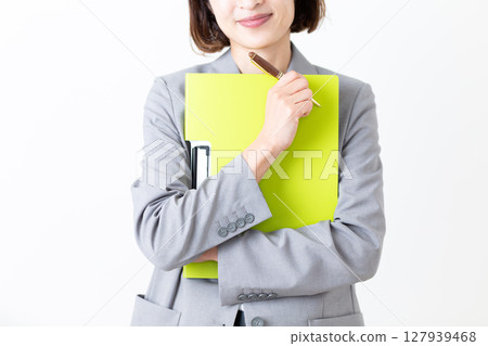 A middle-aged woman in a suit smiling while holding a file A middle-aged woman in a suit smiling while holding a file 127939468