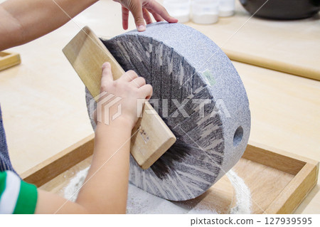 A child (7 years old/boy) scooping out buckwheat flour from a stone mill 127939595