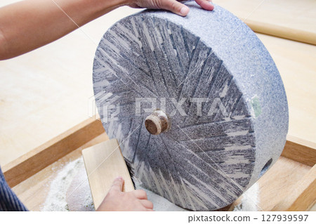 一名兒童(7歲/男孩)從石磨中舀出蕎麥粉 一名兒童(7歲/男孩)從石磨中舀出蕎麥粉 127939597