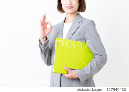 一位身著西裝的中年婦女拿著文件，做著圓圈手勢 127940480