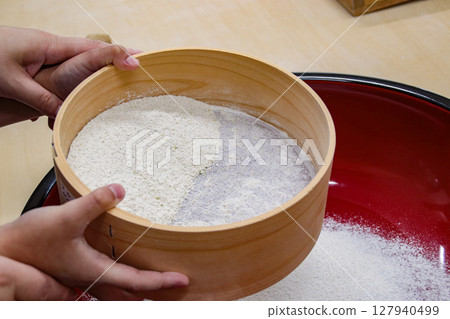 A child (7 years old/boy) sifting buckwheat flour with an adult A child (7 years old/boy) sifting buckwheat flour with an adult 127940499