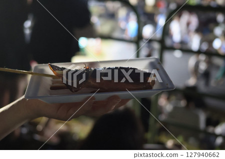 Grilled squid purchased from a food stall with the night view in the background Grilled squid purchased from a food stall with the night view in the background 127940662