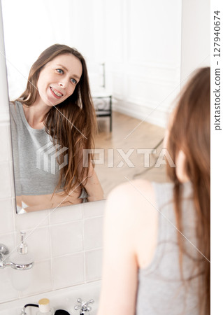 A beautiful young woman with braces looks in the mirror and smiles at her reflection. A beautiful young woman with braces looks in the mirror and smiles at her reflection. 127940674