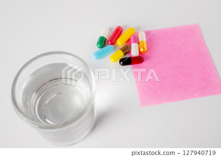 Top view of glass of water, many pill capsules and pink note paper on white background with copy space. 127940719