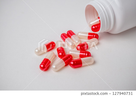 Close up bottle container with red and white medication capsules on white background with copy space. 127940731