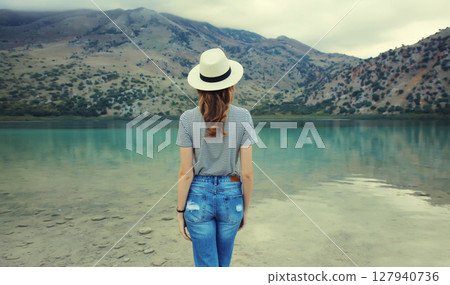 Summer vacation, young woman tourist standing and looking on lake and mountains background 127940736