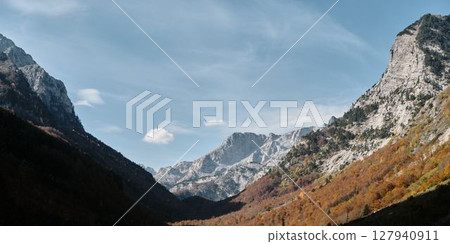 Sharp ridges and colorful forested slopes of the Prokletije mountains in autumn, captured in warm light under a clear blue sky. Nature of Montenegro 127940911