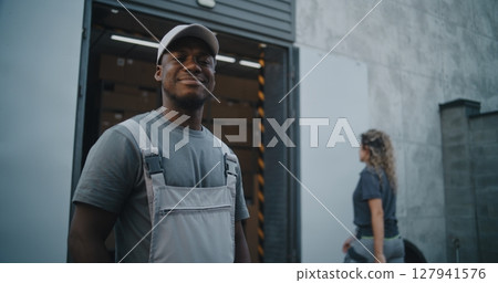 Outside of Logistics Warehouse: Worker Giving Cardboard Box to Colleague, Looking at Camera 127941576