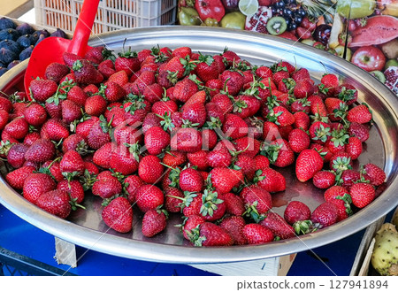 Fresh strawberries displayed on a silver tray at a vibrant market with colorful fruits around Fresh strawberries displayed on a silver tray at a vibrant market with colorful fruits around 127941894