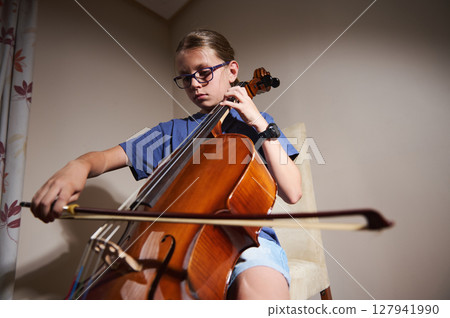 Young Musician Practicing the Cello in Warm Indoor Light 127941990