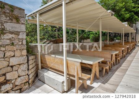 Outdoor cafe terrace with wooden benches under canopy. 127942018
