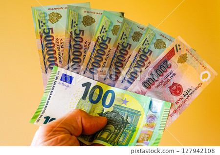 Vietnam dong and euro banknotes, held in hands, yellow background, equivalent international exchange 127942108