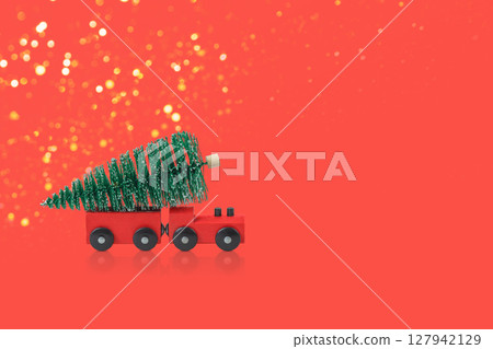 Winter fairy tale composition of green Christmas trees and red steam train carrying Christmas tree on red background. Concept of Christmas, holiday, congratulations 127942129