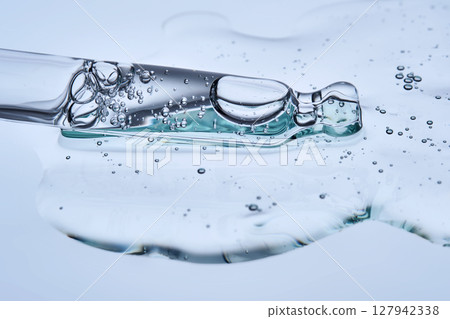 The texture of the facial serum with bubbles and an eyedropper on a blue background. The texture of the facial serum with bubbles and an eyedropper on a blue background. 127942338
