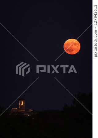 Illuminated church tower, reddish full moon. 127942512