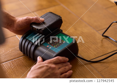 A handyman is actively installing various equipment using a powerful drill on a wooden floor 127942545