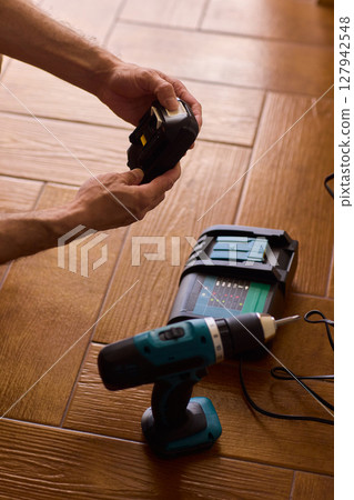 A handyman is actively installing various equipment using a powerful drill on a wooden floor 127942548