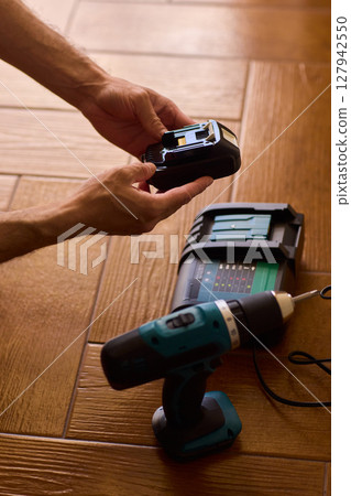 A handyman is actively installing various equipment using a powerful drill on a wooden floor A handyman is actively installing various equipment using a powerful drill on a wooden floor 127942550