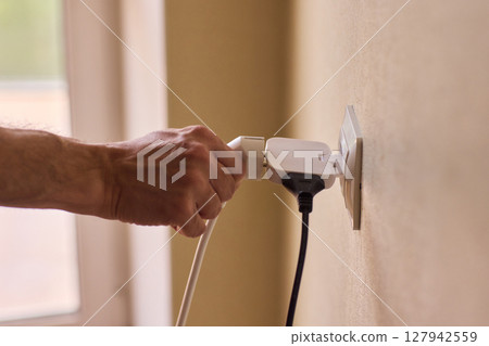 Manually plugging an electrical device into a wall outlet for convenient use and power Manually plugging an electrical device into a wall outlet for convenient use and power 127942559