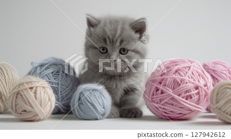 Cute gray kitten surrounded by knitting yarn balls on a light background, creating a delightful scene 127942612