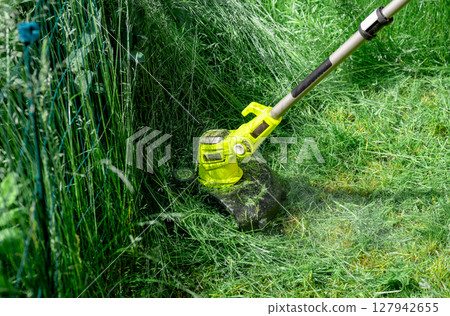 man trimming overgrown grass with electric string trimmer in summer garden man trimming overgrown grass with electric string trimmer in summer garden 127942655