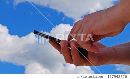 Close up unknown hands of man holding phone, using apps. outdoors near sky background. Hands holding smartphone 127942726