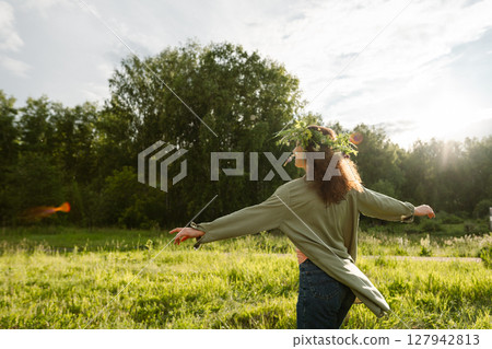 Female with floral crown dancing in countryside field outdoors, back view. Symbol of carefree freedom, unplugged relaxation, eco lifestyle and mindfulness in nature 127942813