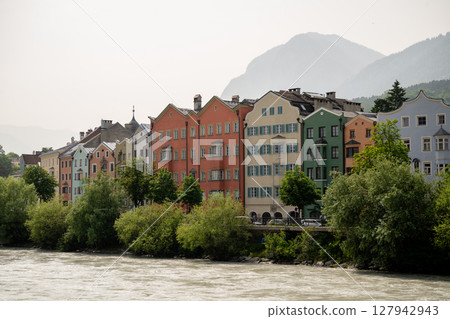 Colorful historic houses along Inn River in Innsbruck, Austria with mountain backdrop 127942943