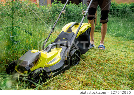 Man mowing overgrown lawn with yellow electric mower near wooden house steps Man mowing overgrown lawn with yellow electric mower near wooden house steps 127942950