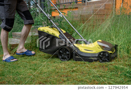 Man mowing overgrown lawn with yellow electric mower near wooden house steps Man mowing overgrown lawn with yellow electric mower near wooden house steps 127942954