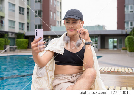 Non-binary person relaxing in poolside during summer wearing sport bra 127943013