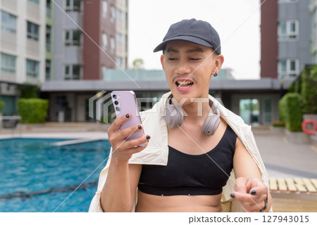 Non-binary person relaxing in poolside during summer wearing sport bra 127943015