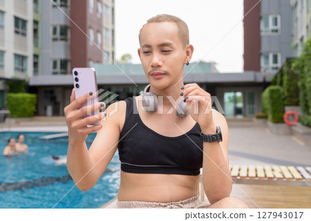 Non-binary person relaxing in poolside during summer wearing sport bra 127943017