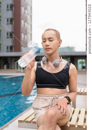 Non-binary person relaxing in poolside during summer wearing sport bra Non-binary person relaxing in poolside during summer wearing sport bra 127943028