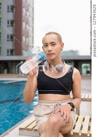 Non-binary person relaxing in poolside during summer wearing sport bra Non-binary person relaxing in poolside during summer wearing sport bra 127943029
