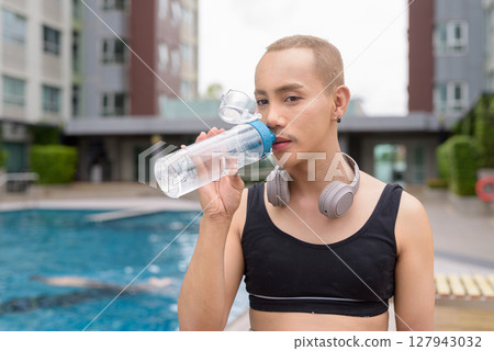 Non-binary person relaxing in poolside during summer wearing sport bra 127943032