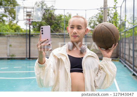 Queer non-binary model holding basketball outdoors 127943047
