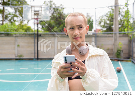 Queer non-binary model outdoors in basketball court texting with phone 127943051