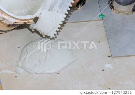 Worker spreads drying mortar on floor in preparation for tile installation in newly renovated space. Worker spreads drying mortar on floor in preparation for tile installation in newly renovated space. 127943231