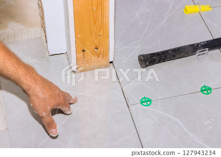 Hand of worker aligns tiles on floor while preparing for next step in home renovation. 127943234