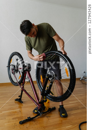 Vertical shot of cyclist male wiping dusty dirty tire of bicycle wheel with cloth, detailing bicycle at home showing commitment to cycling maintenance and equipment care. Concept of bike service Vertical shot of cyclist male wiping dusty dirty tire of bicycle wheel with cloth, detailing bicycle at home showing commitment to cycling maintenance and equipment care. Concept of bike service 127943426