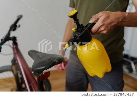 Bicycle male cleaning bicycle saddle, spraying water during detailed maintenance in professional workshop, focusing on bike hygiene and precision care process, close-up. Concept of bike service. 127943437