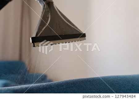 Close-up cropped shot of unrecognizable man cleaning blue sofa with washing vacuum cleaner designed for furniture, ensuring deep cleaning and sanitizing for fresh hygienic home environment, closeup 127943484