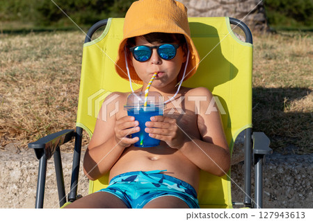 Boy in panama and sunglasses drinking blue beverage on a sunny summer day Boy in panama and sunglasses drinking blue beverage on a sunny summer day 127943613