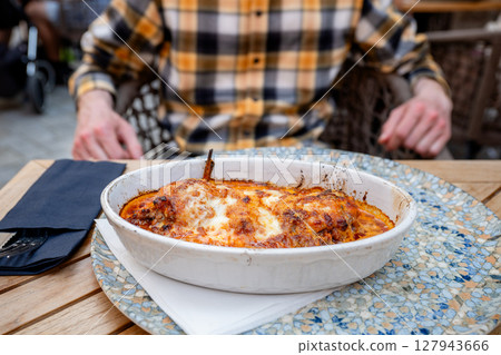 Baked pasta Bolognese with melted cheese in ceramic dish on restaurant table 127943666